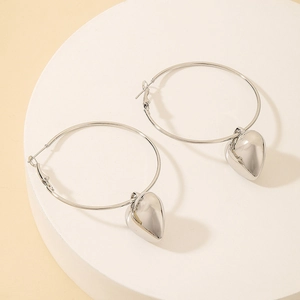 Polished silver heart charms hanging from large metallic hoop earrings on a white stand