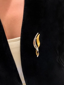 Macro detail of bicolored wavy brooch with brushed metal texture on a black blazer