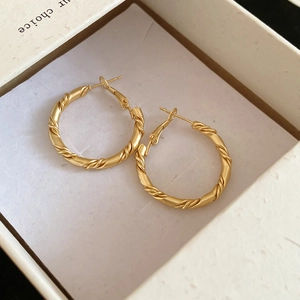 Close-up of golden twisted hoop earrings with textured matte finish in a gift box