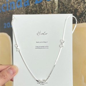 Detailed view of silver snake chain necklace featuring three delicate bow pendants