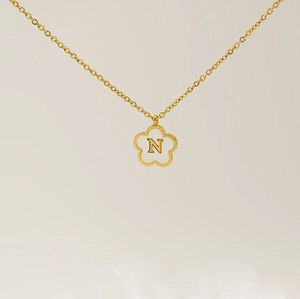 Close-up of golden clover pendant featuring letter N on white shell background