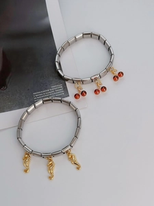 Detail of stainless steel modular bracelets with red cherry and gold seahorse charms