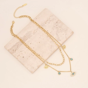 Layered gold evil eye necklace with turquoise beads on a minimalist stone texture background
