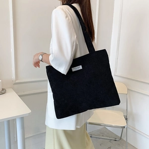 Detail view of black corduroy tote bag with fashion label on shoulder of model