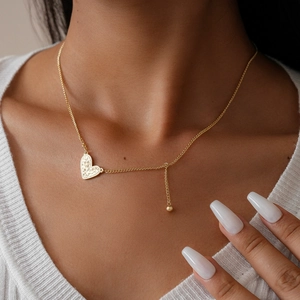 Close-up of gold heart pendant necklace with textured finish and ball tassel on a model