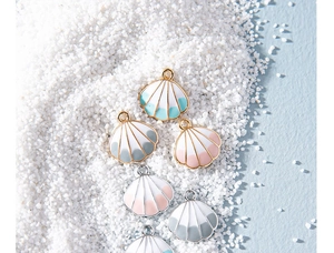 Macro shot of colorful enamel shell pendants with gold and silver edges on white sand
