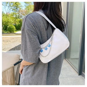 Close-up of white shoulder bag featuring a blue butterfly pendant and silver chain