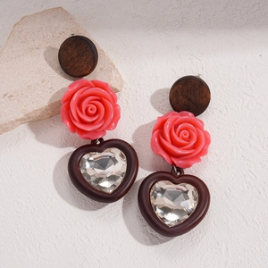 Détail de boucles d'oreilles bohèmes avec rose en résine et pendentif cœur cristal