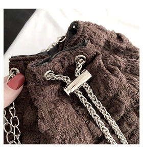 Detail of brown pleated bucket bag with silver metal chain drawstring closure