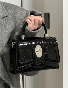 Close-up of black patent leather crossbody bag with crocodile texture and silver turn-lock