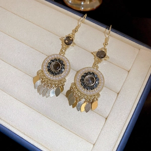 Detail of bohemian gold earrings with dark crystal, pearls and leaf tassels in box