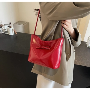 Side view of a glossy red shoulder bag with bow detail worn by a model in a cafe