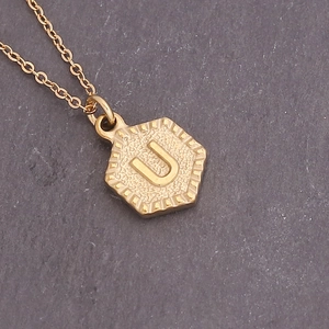 Macro detail of a golden hexagonal pendant necklace featuring the engraved letter U
