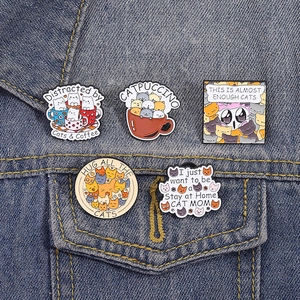 Set of 5 colorful cartoon cat enamel pins displayed on dark blue denim jacket fabric
