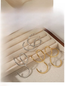 Detailed view of silver and gold irregular twisted line earrings on beige velvet background