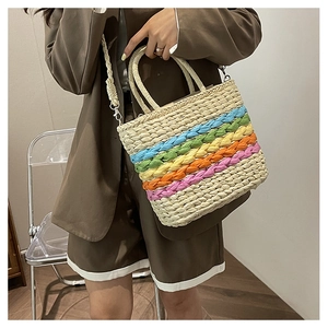Detail of a rainbow striped straw handbag with dual top handles and detachable shoulder strap