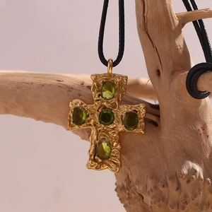 Macro detail of hammered 18K gold cross pendant with green gems on vintage wood