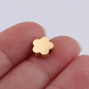 Macro view of a small golden five-petal flower bead held between fingertips for DIY jewelry