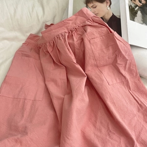 Detail shot of a pink cotton apron featuring large side pockets on natural bedding