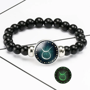 Detail of hand-woven black leather bracelet showing luminous Taurus zodiac charm glow