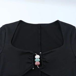 Dettaglio dello scollo quadrato con perline decorative in marmo su un vestito nero in maglia