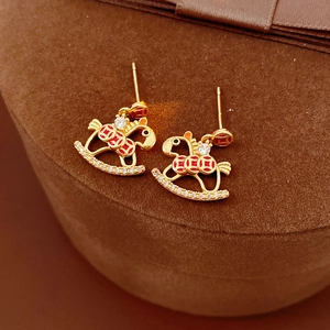Detail of rocking horse earrings with red enamel and pavé stones on a velvet box
