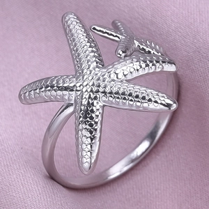Macro detail of silver starfish ring with textured granules on pink satin background