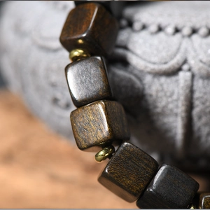 Dark brown square wooden bead bracelet with gold spacers on a zen stone background