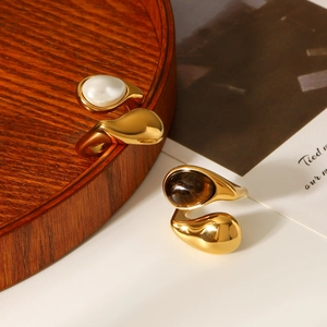 Detailed shot of teardrop tiger eye and pearl gold rings on a rustic wooden plate