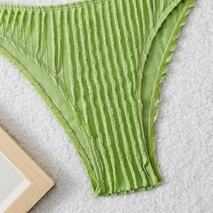 Detailed view of avocado green bikini bottoms with textured fabric on plush background