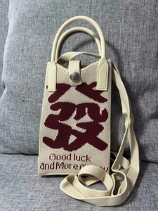 Close-up of beige knit phone bag with red Good Luck embroidery on a grey sofa