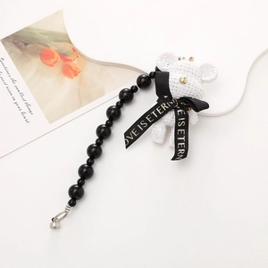 Close-up of a white plush bear keychain with black LOVE IS ETERN ribbon and bead chain