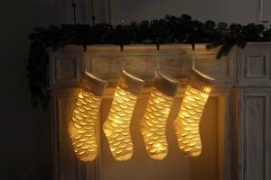 Close-up of four white knit Christmas stockings with fish scale pattern and LED lights