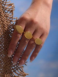 Detail of a triple oval linked gold ring shown worn on fingers with a beach background