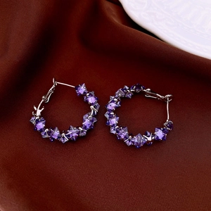 Macro detail of silver hoop earrings with purple geometric crystals on silk fabric