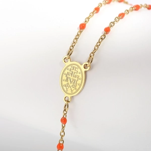 Macro detail of gold rosary necklace with orange beads and engraved religious oval charm