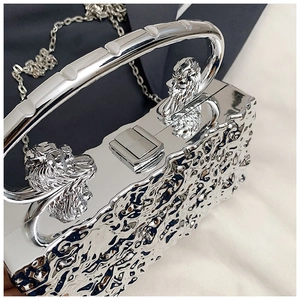 Detail of silver acrylic evening bag featuring hammered texture and lion head metal handles
