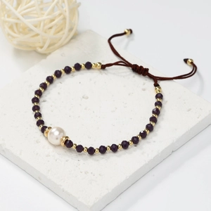 Close-up of handmade purple crystal bead bracelet with a central white pearl and gold accents