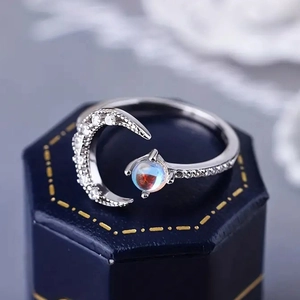 Macro detail of silver moon ring with iridescent stone on a blue velvet jewelry box