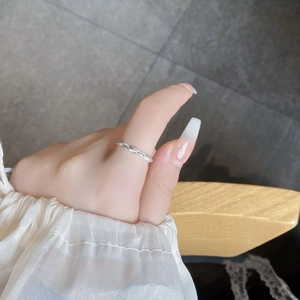 Detail eines silbernen geflochtenen Rings am Finger mit elegantem weißem Ärmel