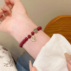 Dettaglio del bracciale con perle rosso scuro e ciondolo dorato con carattere Fu