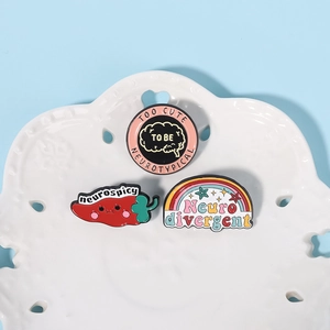 Three enamel pins including a pink circle, red chili, and rainbow on a white decorative tray
