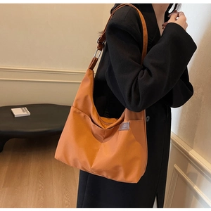 Detail view of large orange nylon tote bag with fashion label and shoulder strap