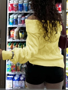 Rear view of yellow off-shoulder cable knit sweater paired with black shorts and tights