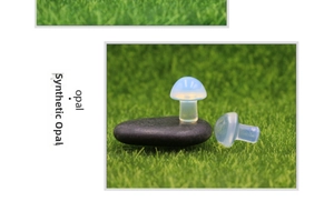 Mini synthetic opal mushroom stone figurine on black pebbles with green grass background