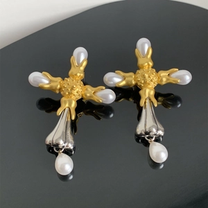 Detailed view of vintage-style gold and silver cross earrings with pearl on a mirror surface