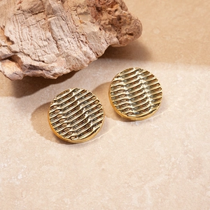 Macro shot of gold circular earrings with ripple texture on a beige stone surface