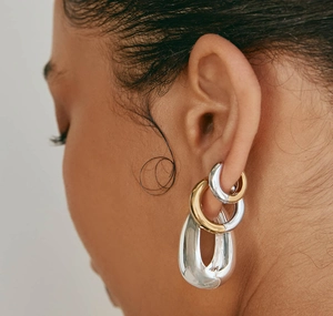 Close-up of model wearing layered gold and silver textured hoop earrings with metallic finish