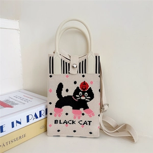 Detail of knitted beige cat bag showing black cat pattern and texture of woven fabric
