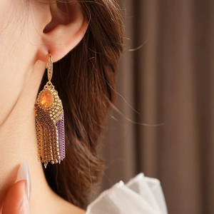 Detail of bohemian gold tassel earring with orange teardrop stone on model ear